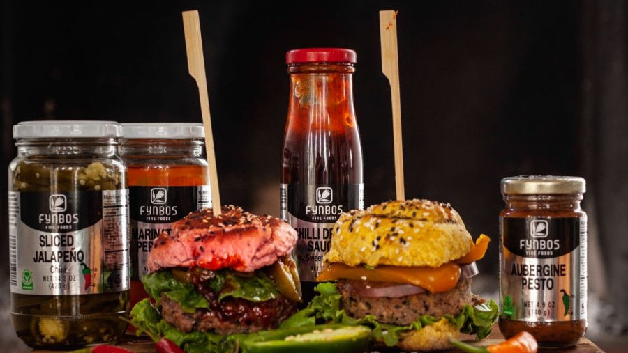 Two burgers with various jars of Fynbos food products on a wooden board.